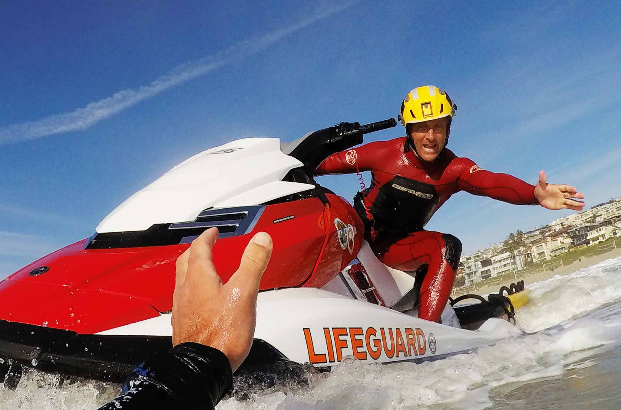 Lifeguard helping a swimmer in the water while riding a jetski.